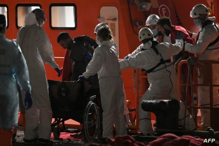 Emergency personnel assist exhausted migrants in the port of Arguineguin, after their rescue at the coast of the Canary island of Gran Canaria, Spain, on November 18, 2021. - Migrant crossings from North Africa into Spain have surged this year, with many people risking their lives on dangerous boat journeys across the Mediterranean. Some 16,827 migrants have arrived in the Canaries between January and October, an increase of 44 percent from the same period a year ago, according to Spain's interior ministry. (Photo by LLUIS GENE / AFP)