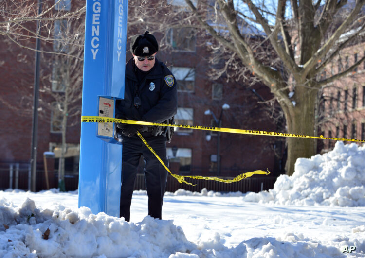 A police officer ties tape to secure an area at Harvard University in Cambridge, Mass., Monday, Dec. 16, 2013. Four buildings on campus were evacuated after campus police received an unconfirmed report that explosives may have been placed inside, interrupting final exams. (AP Photo/Josh Reynolds)
