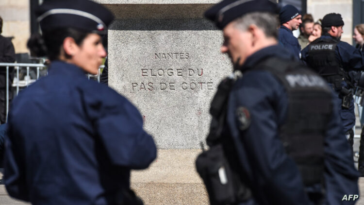French police officers stand by a monument bearing the inscription "Nantes: Ode to the side-step" during a demonstration against the Universal National Service, or SNU (Service National Universel) held at a promotional campaign village for the SNU, in Nantes, Western France, on April 19, 2023. (Photo by Sebastien SALOM-GOMIS / AFP)